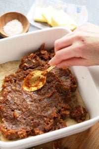 A person effortlessly prepares easy pecan pie bars by pouring a spoonful of pecans into a baking dish.