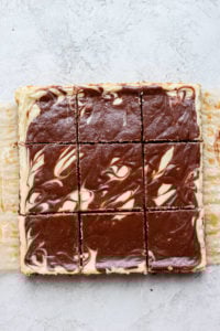 white swirled bars atop a square of chocolate cheesecake on a white surface.