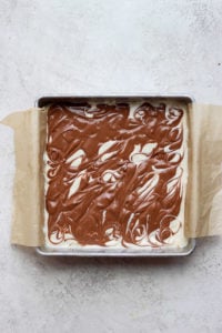 Cheesecake bars with chocolate icing in a baking pan.