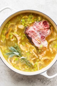 A pot of soup with meat, peas and sprigs of rosemary.