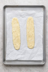 Two unbaked dough logs placed on a parchment-lined baking sheet, ready to be baked.