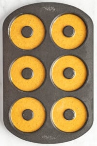 A six-cavity donut baking pan filled with pumpkin batter, ready for baking.
