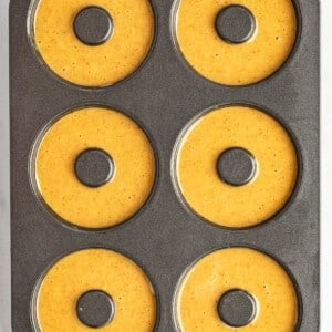 A six-cavity donut baking pan filled with pumpkin batter, ready for baking.