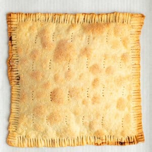 A baked, rectangular pie with crimped edges, small perforations on the top, and a golden-brown crust, placed on parchment paper.