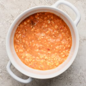 A white ceramic bowl filled with creamy tomato soup, placed on a textured light gray surface.