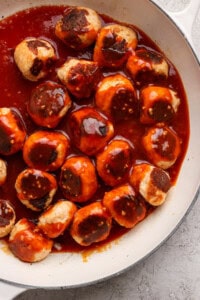 Meatballs in a skillet covered with a reddish-brown sauce.