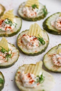 Cucumber slices topped with sour cream, a potato chip, dill, and paprika, arranged on a plate.