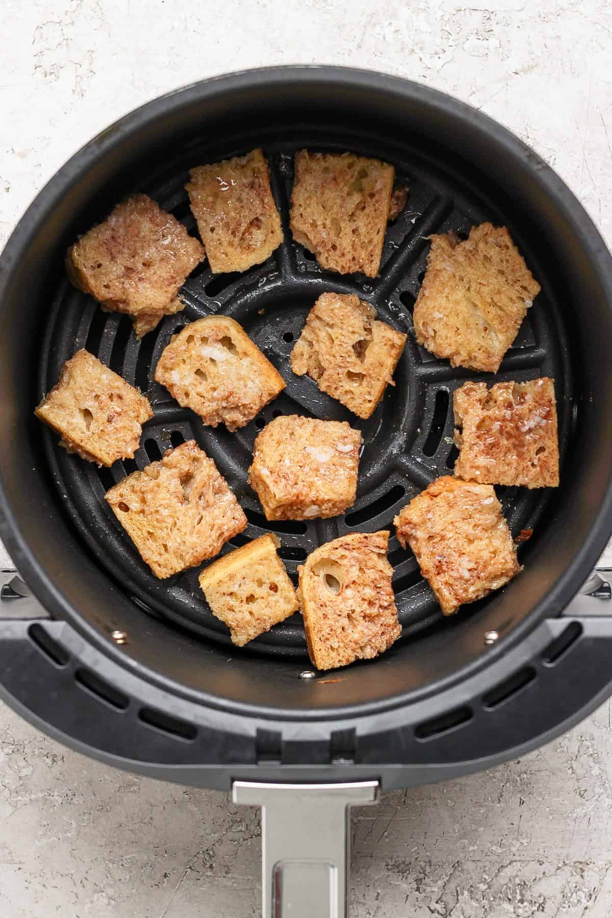 Pieces of bread being toasted in an air fryer basket.