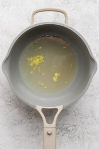 A gray saucepan filled with water and small yellow floral bits on a textured light gray surface.