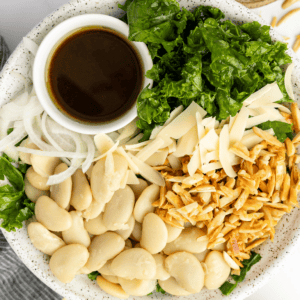 A plate with butter beans, sliced onions, kale, shredded cheese, toasted slivered almonds, and a small cup of dark dressing.