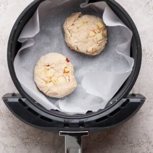 Two unbaked dough rounds with visible chunks, placed on parchment paper inside an air fryer basket.
