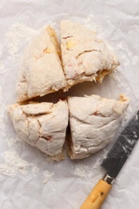 Round ball of uncooked dough cut into four equal pieces on floured parchment paper, with a knife placed beside it.