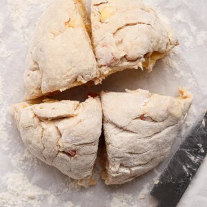 Round ball of uncooked dough cut into four equal pieces on floured parchment paper, with a knife placed beside it.