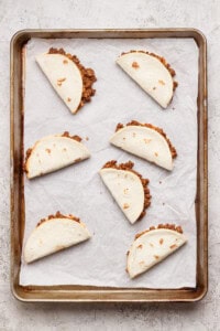 Six folded flour tortillas filled with ground beef are arranged on a parchment-lined baking sheet.