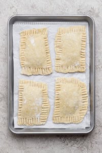 Four unbaked rectangular hand pies with crimped edges are arranged on a parchment-lined baking sheet.
