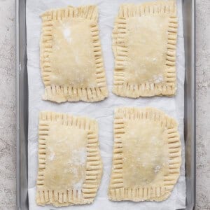 Four unbaked rectangular hand pies with crimped edges are arranged on a parchment-lined baking sheet.