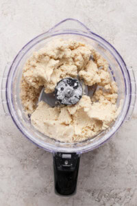 A food processor filled with partially mixed dough sits on a light-colored countertop.