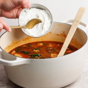 A person pouring cream into a pot of soup.