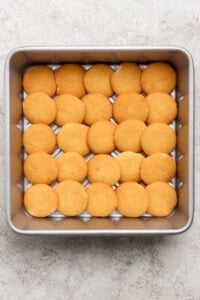 A square baking pan filled with a single layer of round vanilla wafer cookies arranged in a grid pattern.
