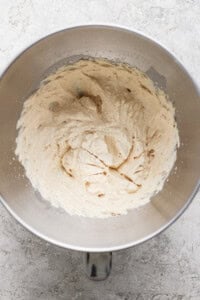 A metal mixing bowl containing light-colored creamed mixture, likely butter and sugar, on a textured gray surface.
