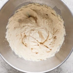 A metal mixing bowl containing light-colored creamed mixture, likely butter and sugar, on a textured gray surface.